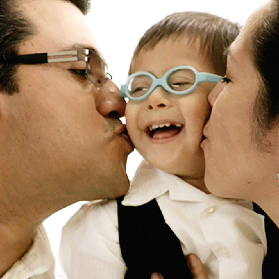 An RMHC family, the Acostas, with parents kissing their smiling child in glasses
